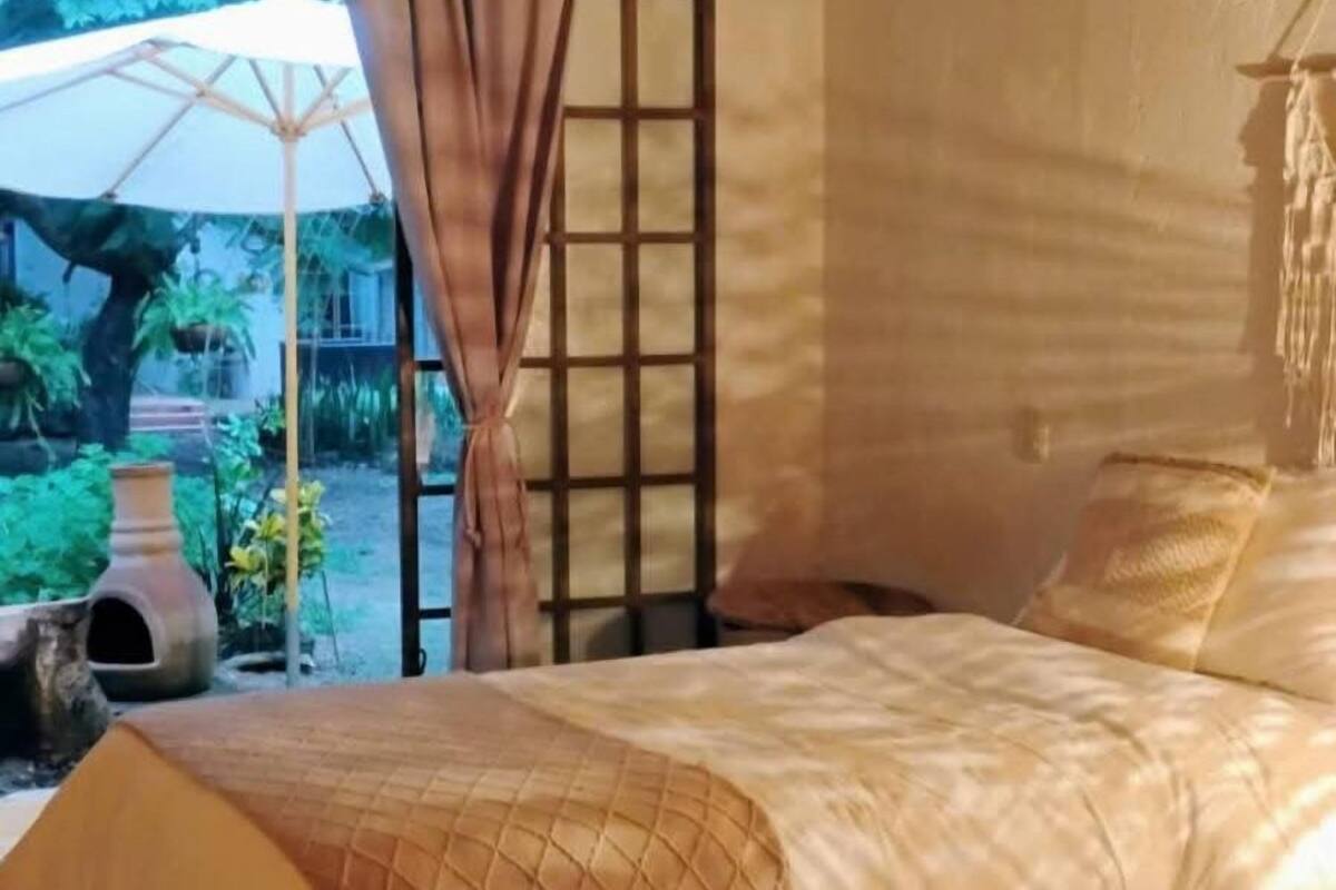 Um quarto com uma cama coberta por um edredom estampado, uma janela com vista para o verde lá fora e uma porta com design em grade.
