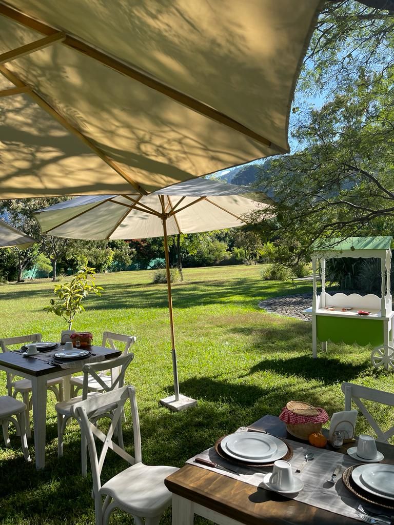 Un área de comedor al aire libre con una mesa dispuesta para cuatro personas, rodeada de sillas blancas, bajo un toldo grande.