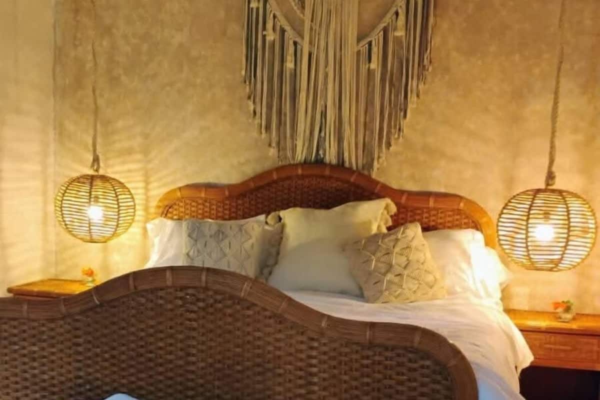 Uma cama com cabeceira de fibra trançada, um banco com toalhas e duas luminárias de mesa.