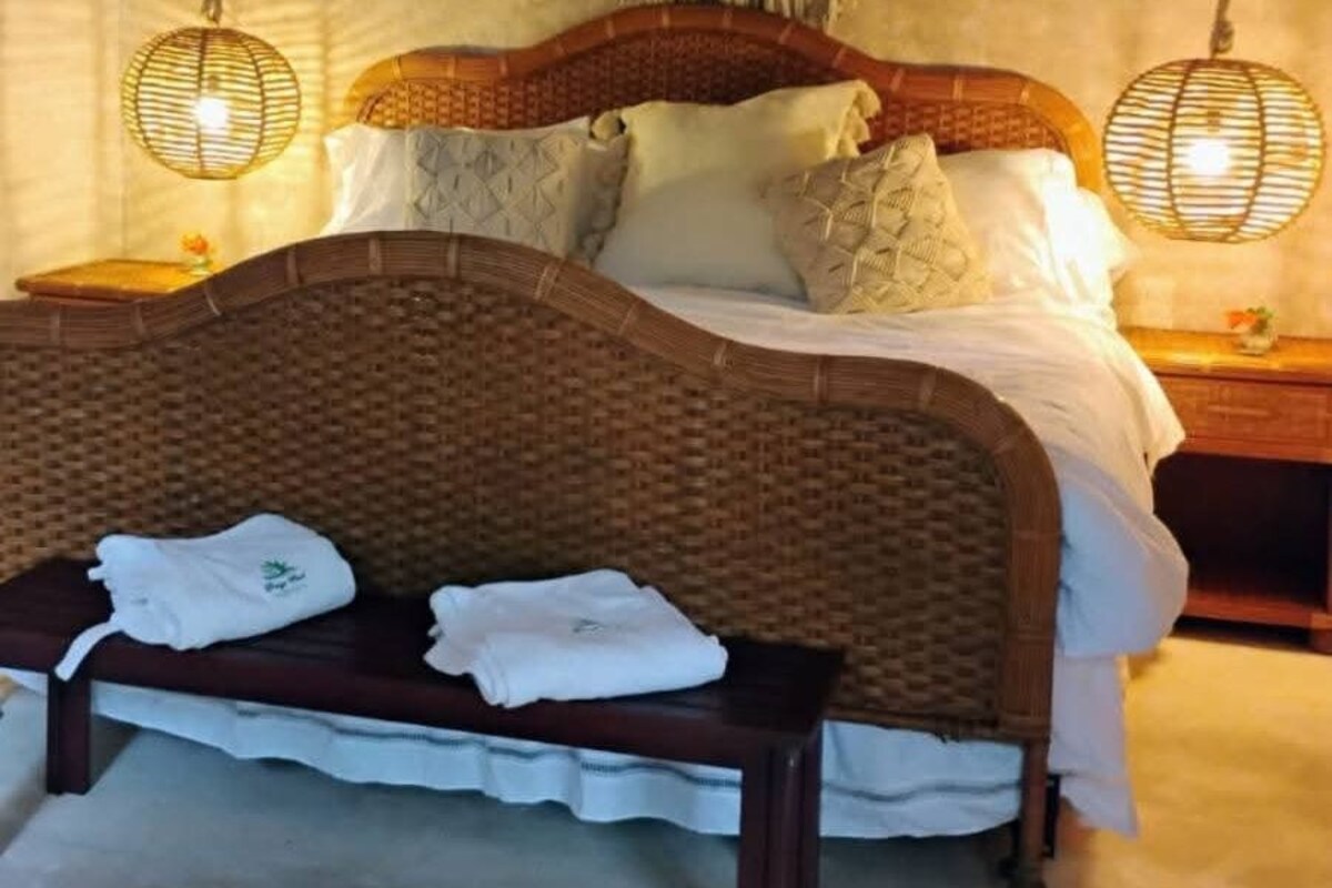 Una cama con cabecera trenzada, un banco con toallas y dos lámparas de noche.