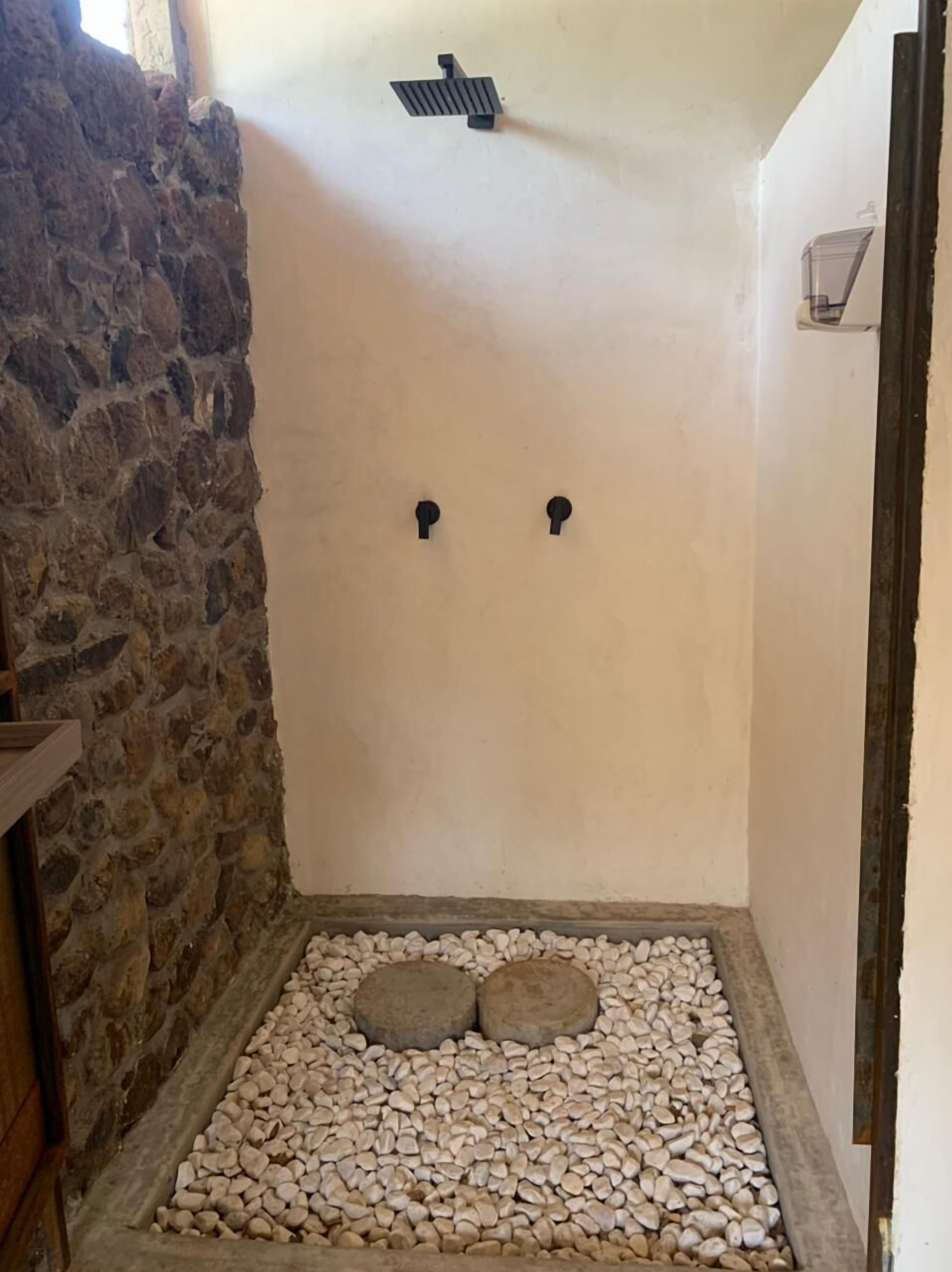 Un’area doccia con pareti in pietra, due maniglie nere e pavimento in ciottoli.