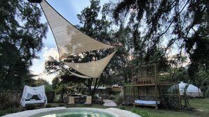 A pool area with a canopy, stone flooring, and a gazebo.