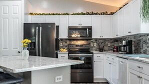 A modern kitchen with white cabinets, a stainless steel refrigerator, a microwave, an oven, and a granite countertop. - Perfect Getaway, Anytime of Year, Sunny, Clean, Spacious & Ideally Located! (Cape Coral)