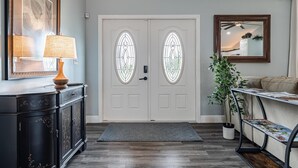 A foyer with a double door, a console table with a lamp, a potted plant, a sofa, and a magazine rack. - Perfect Getaway, Anytime of Year, Sunny, Clean, Spacious & Ideally Located! (Cape Coral)