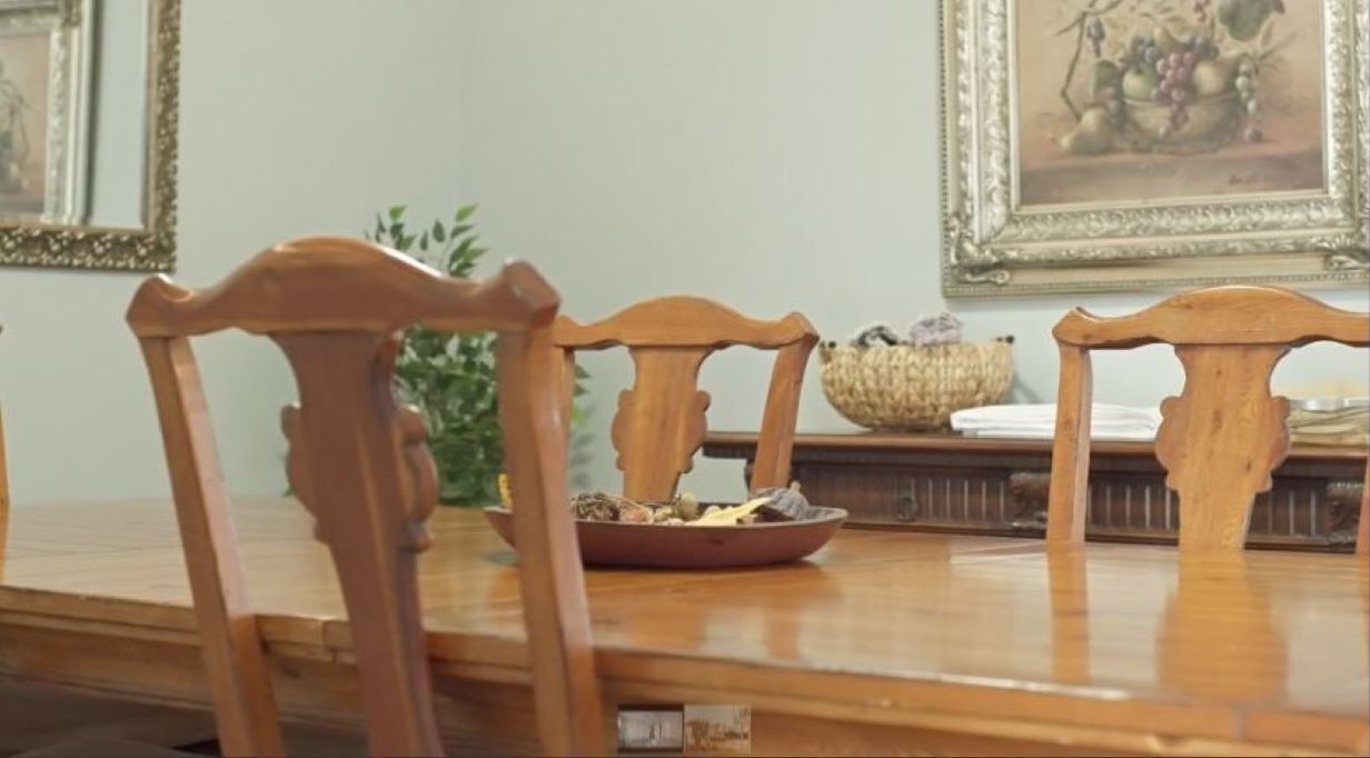 Un tavolo da pranzo in legno con sedie, una ciotola di frutta e quadri appesi al muro.