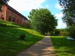 A pathway leading to a brick building with arched windows, surrounded by lush greenery and trees.