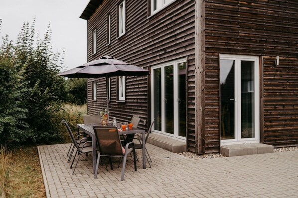 A wooden cabin with a patio, outdoor seating, and a large umbrella.