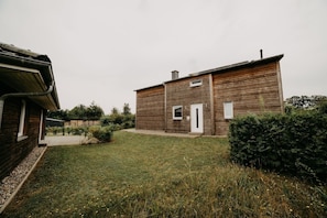 Ein hölzernes Gebäude mit Tür und Fenstern, umgeben von einem grünen Rasen und einigen Büschen.