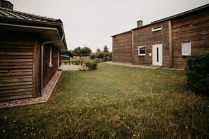 A wooden building with a sloped roof, a small garden with grass and wildflowers, and a paved pathway leading to a door.