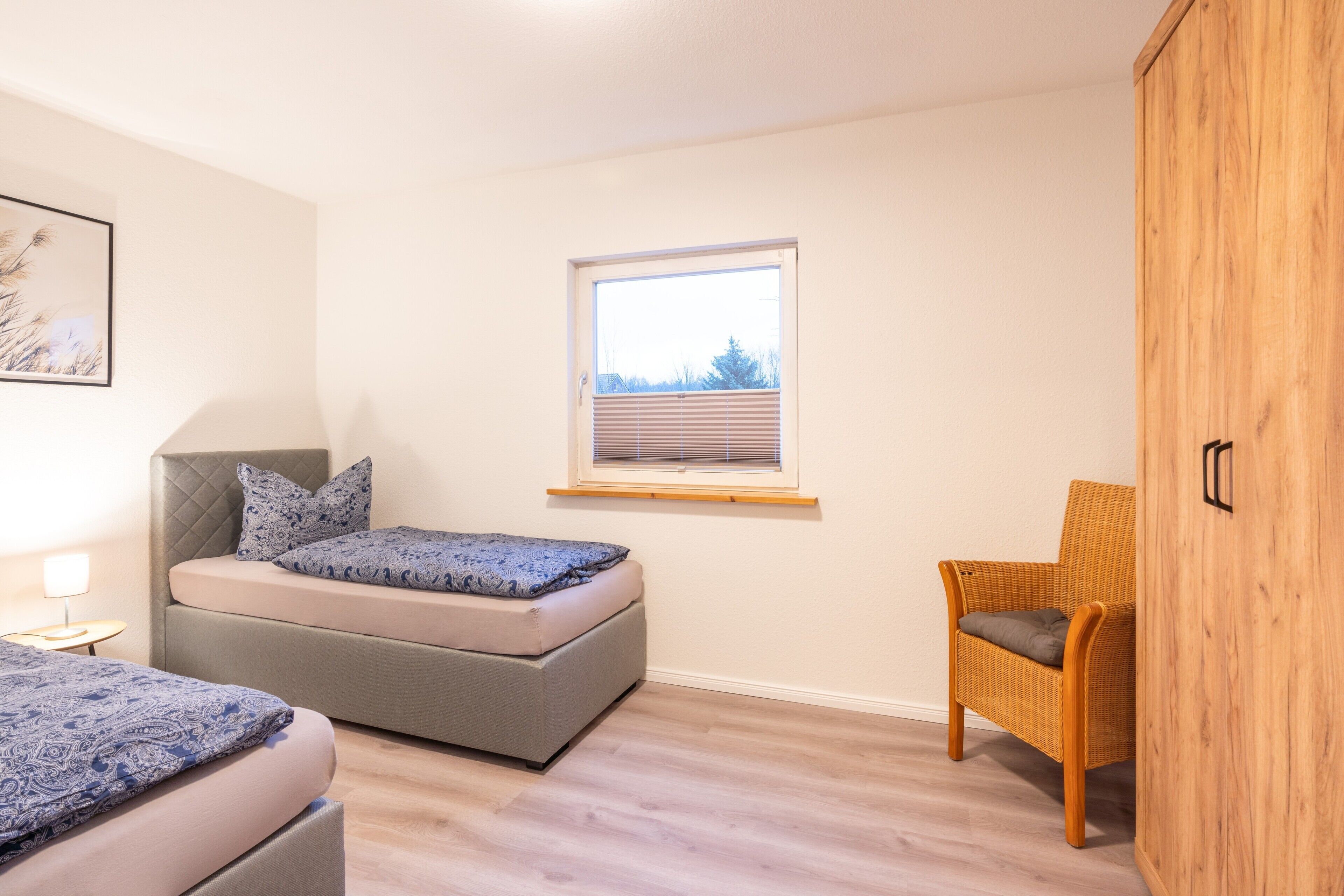 A bedroom with a bed, a chair, a window, and a wooden wardrobe.