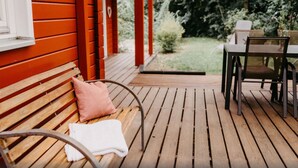 Een houten terras met een bankje en een tafel, omgeven door groen.