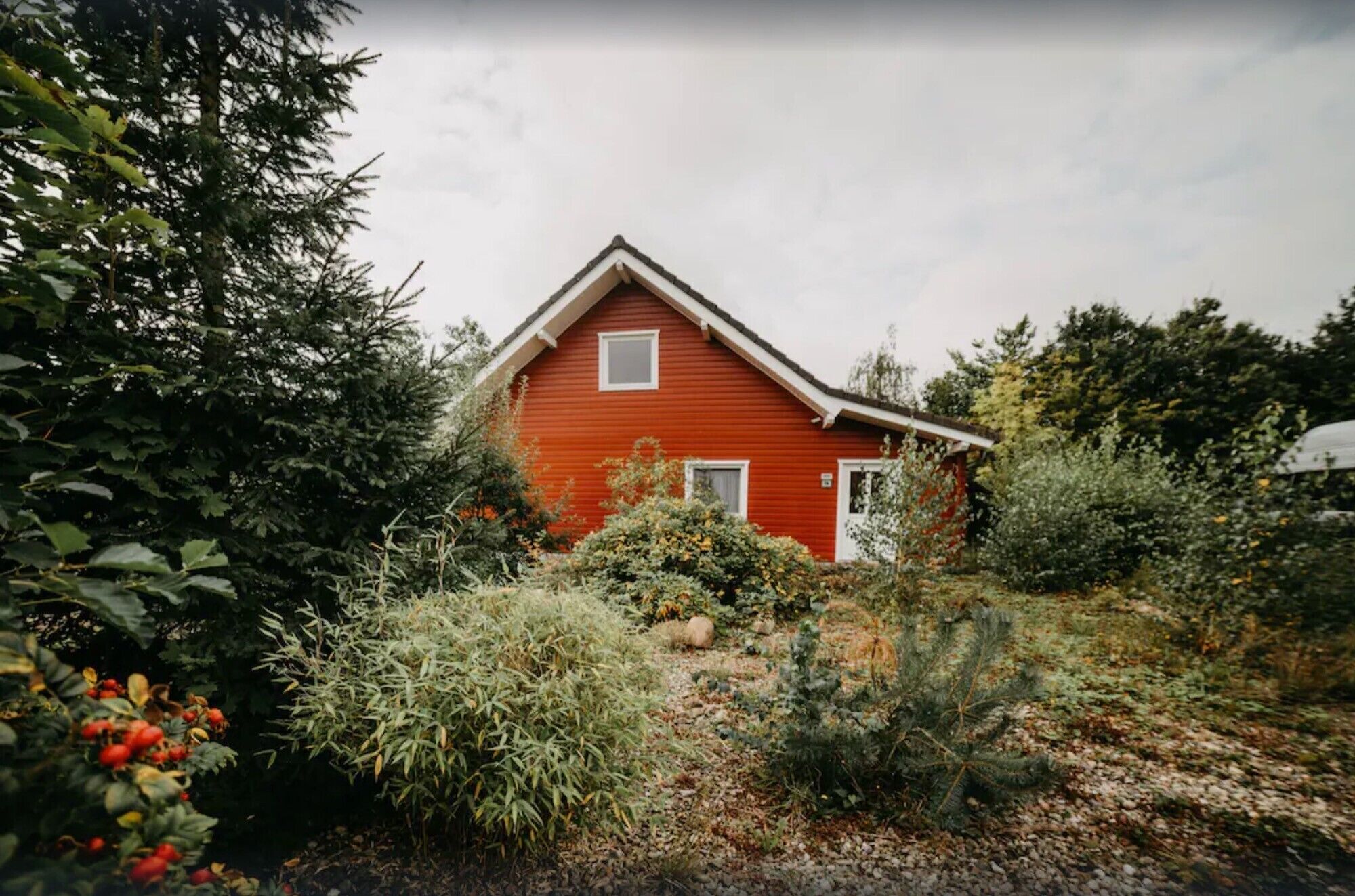 Una casa rossa con tetto a falde circondata da vegetazione lussureggiante.