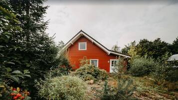 Una casa rossa con tetto a falde circondata da vegetazione lussureggiante.