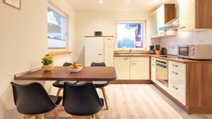 Een moderne keuken met houten kasten, een inbouwoven en een eethoek met een houten tafel en zwarte stoelen.