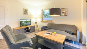 Een moderne woonkamer met een bank, een televisie, een salontafel en een lamp.