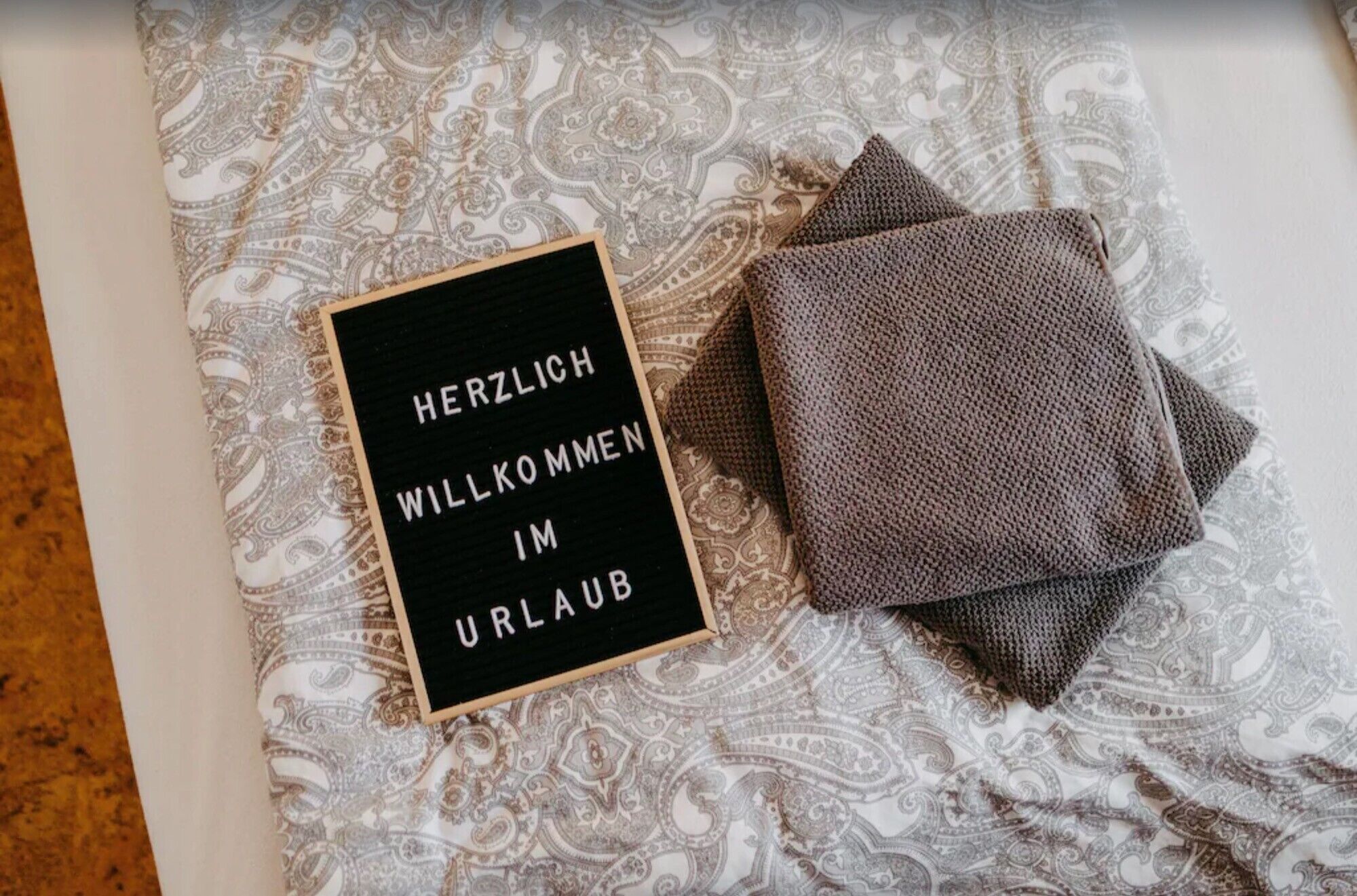 A bed with a patterned bedspread and a black sign with white text.