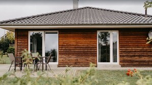 Une maison en bois avec un toit en tuiles, des portes coulissantes en verre et une terrasse avec des chaises.
