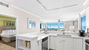 A modern kitchen with white cabinetry, a dishwasher, and a large island. There is a view of the ocean through the windows. - Relaxing Miramar Beach Retreat With Sunset Gulf Views (Miramar Beach)