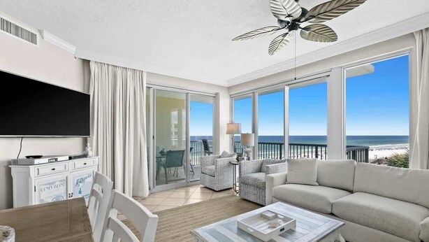 A spacious living room with a large flat-screen TV, a sofa, a coffee table, and a balcony with a view of the ocean. - Relaxing Miramar Beach Retreat With Sunset Gulf Views (Miramar Beach)