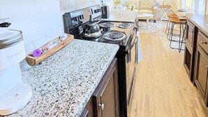 A kitchen with dark wooden cabinets, a granite countertop, a stove, and a coffee maker.