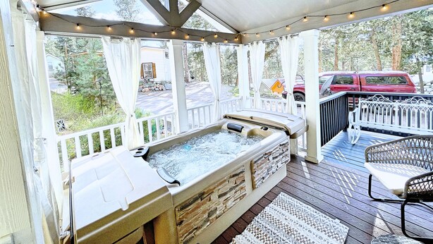 A covered outdoor hot tub area with a wooden deck, a stone bench, and a table with chairs.