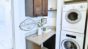 A laundry room with a washing machine and dryer, a wooden cabinet, and a decorative sign.