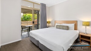 Ein Hotelzimmer mit einem großen Bett, einem Nachttisch, zwei Lampen, einem Balkon mit Blick auf Grünflächen und einem Teppichboden.