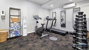 Ein Fitnessraum mit Trainingsgeräten, einem Wasserspender und Ablageflächen.