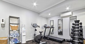 Un gimnasio con equipo de ejercicio, dispensador de agua y estanterías.