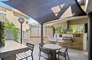 Un patio al aire libre con una mesa redonda y sillas, una parrilla y una zona con sombra.