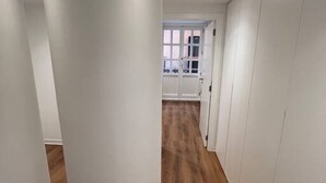 Un couloir aux murs blancs et au plancher en bois qui mène à une porte dotée d’une fenêtre.