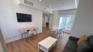 Un salon moderne doté d’un téléviseur à écran plat, d’une table basse blanche, d’un canapé gris et d’un coin repas avec des chaises et une table.