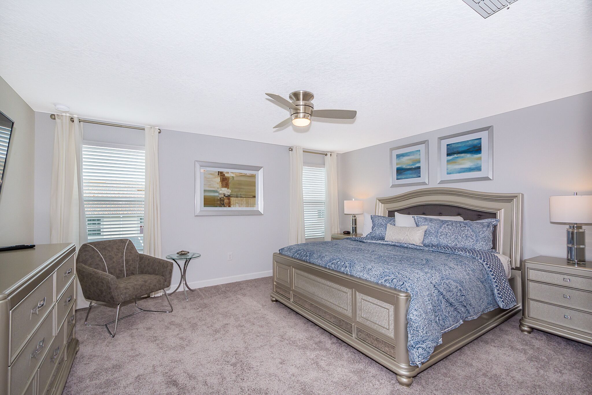 A bedroom with a bed, a chair, a nightstand, a dresser, and a ceiling fan.