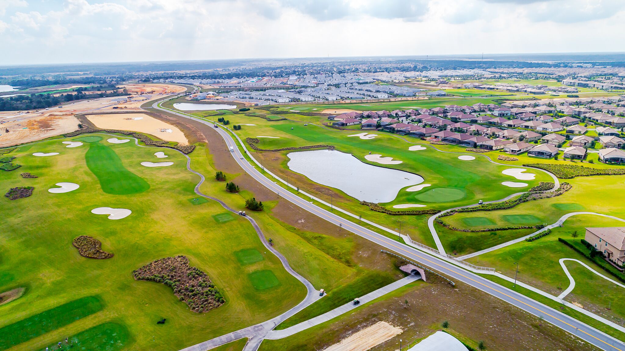 Luchtbeeld van een golfbaan met bunkers, een waterhindernis en een brug.