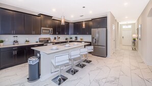 Una cocina moderna con armarios oscuros, electrodomésticos de acero inoxidable y una isla central con taburetes de bar.