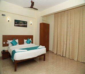 A hotel room with a bed, a wardrobe, a painting, and a ceiling fan. - Royal Chola (Sriperumbudur)
