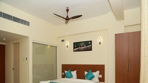 A bedroom with a bed, a wooden wardrobe, a ceiling fan, a wall-mounted light, and a painting. - Royal Chola (Sriperumbudur)