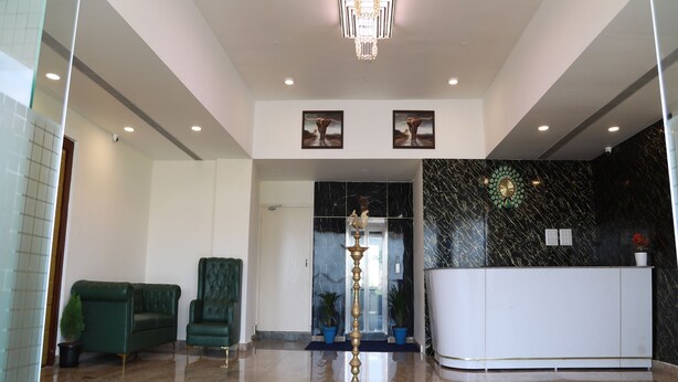 A modern lobby with a reception desk, a green sofa, a tufted armchair, and a decorative floor lamp. - Royal Chola (Sriperumbudur)