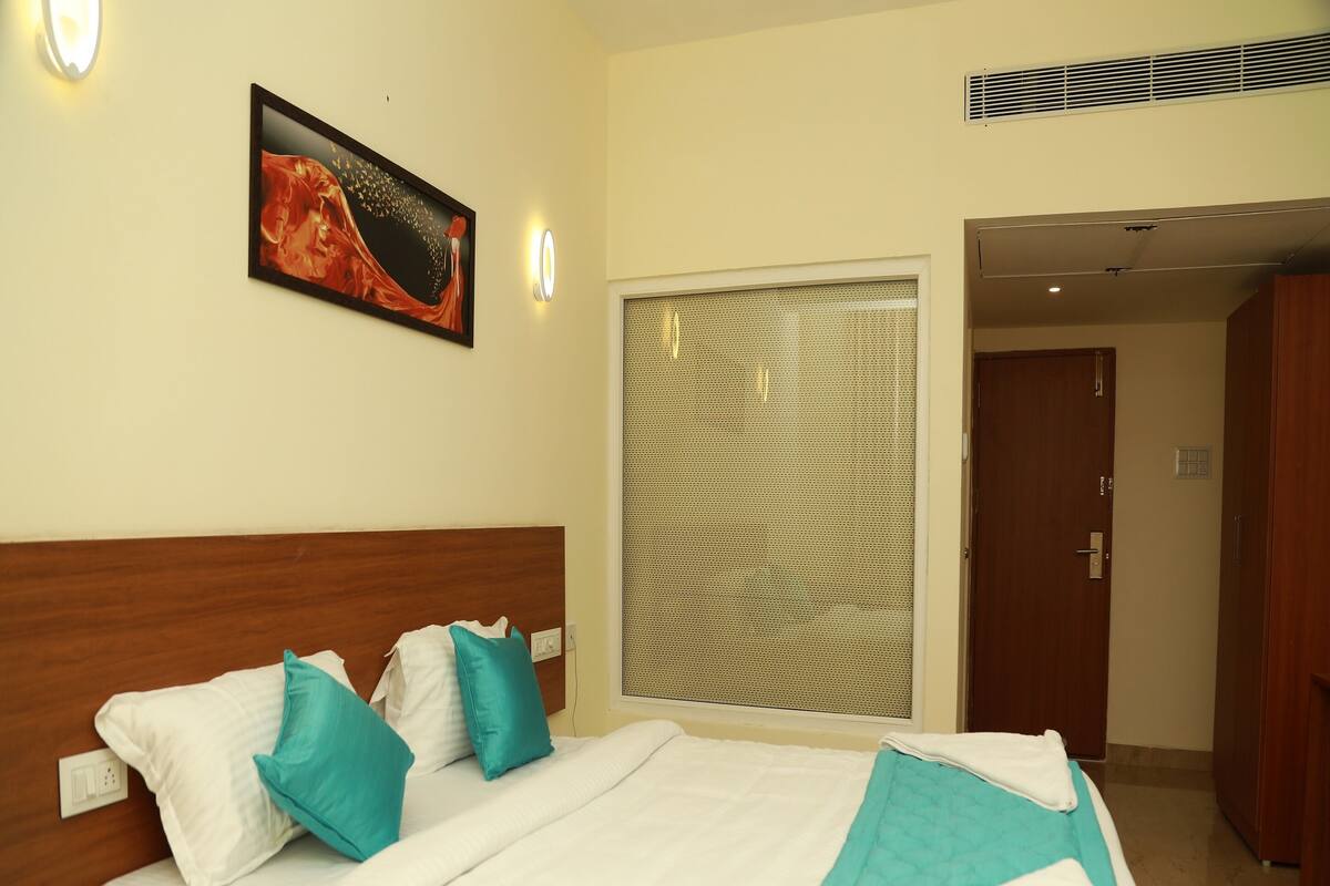 A hotel room with a bed, a painting on the wall, and a window with blinds.