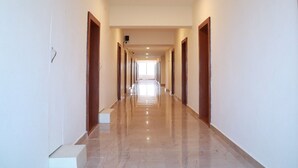 A long, narrow hallway with a polished marble floor, wooden doors on both sides, and a bright light source at the end. - Royal Chola (Sriperumbudur)