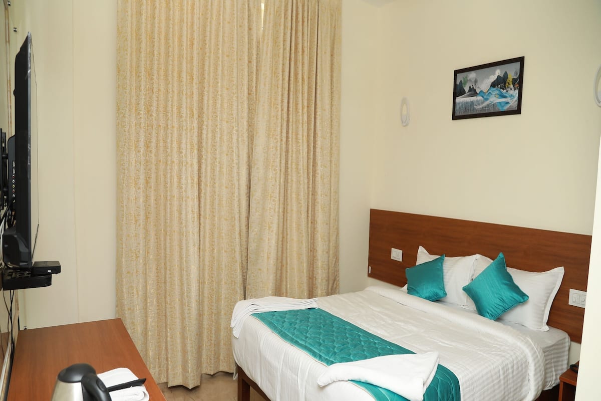 A hotel room with a bed, a desk with a kettle, a television, and a curtain.