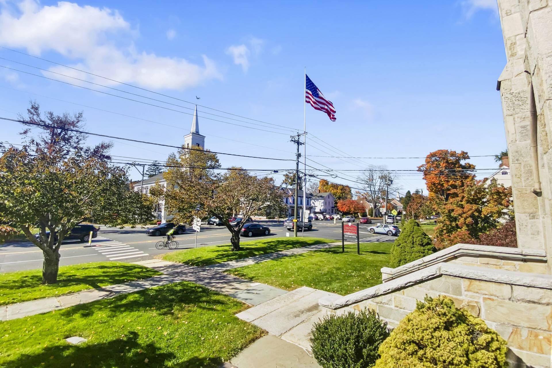 A town square with a flagpole, a crosswalk, and a building with a steeple.