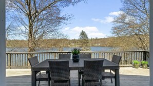 Una terraza con mesa y sillas, con vista a un cuerpo de agua y árboles.