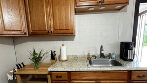 Una cocina compacta con armarios de madera, encimera de granito, pileta y cafetera.