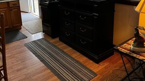 Una cocina con microondas, tostadora y licuadora sobre una encimera negra, una silla de madera y una alfombra en el suelo.