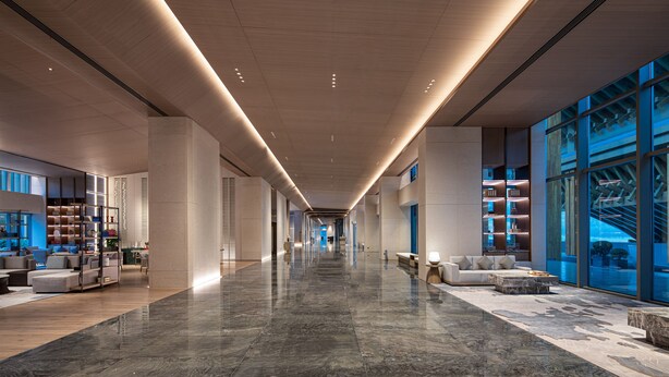 A spacious hotel lobby with a long corridor, modern furnishings, and large windows offering views of the outside. - NBICC Wonderland Hotel (Ningbo)