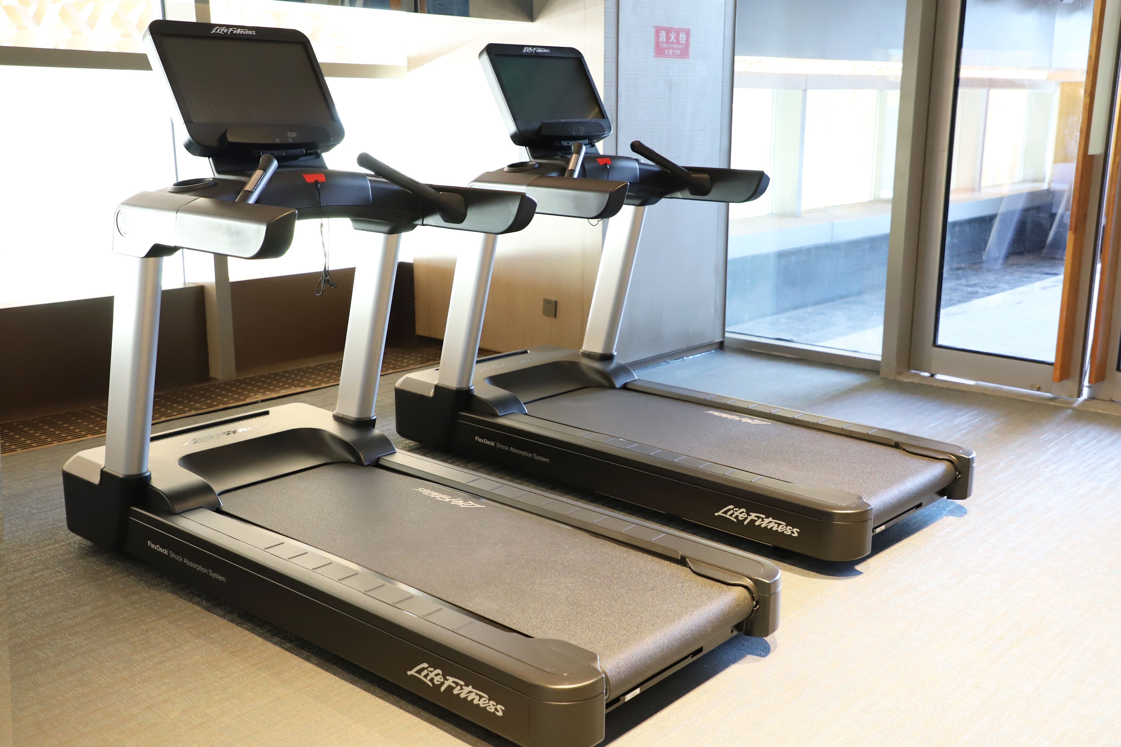 Two Life Fitness treadmills in a gym with a large window in the background.