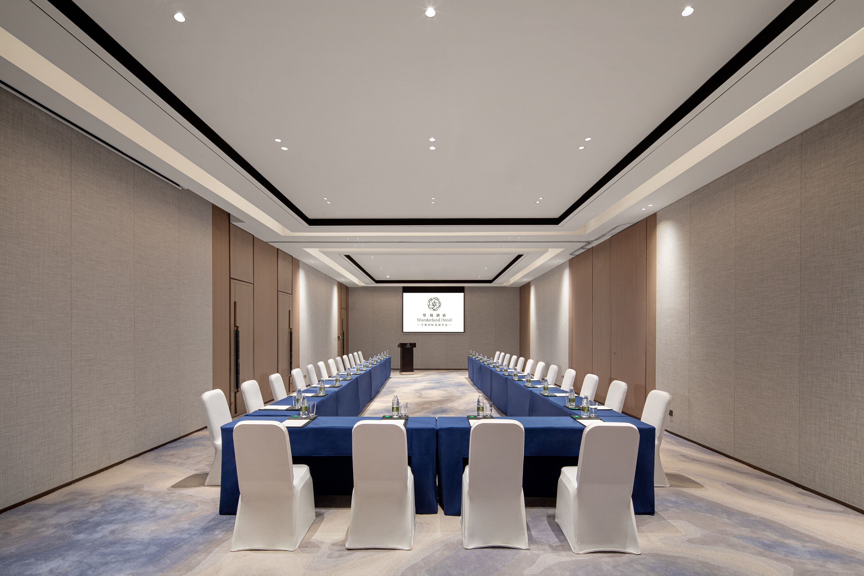 A conference room with a long table, white chairs, and a projector screen at the front.