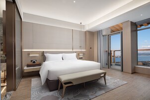 Un dormitorio moderno con una cama grande, un banco, una mesita de noche y vista al mar a través de una puerta corredera.