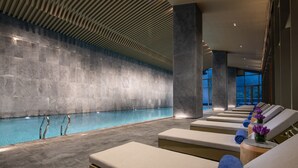 A modern indoor pool with clear water, surrounded by lounge chairs with towels. - NBICC Wonderland Hotel (Ningbo)